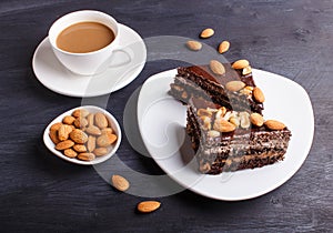 Chocolate cake with caramel, peanuts and almonds on a black wooden background