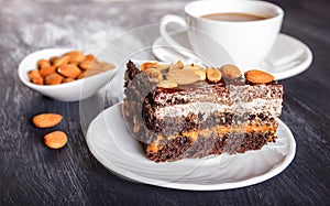 Chocolate cake with caramel, peanuts and almonds on a black wooden background