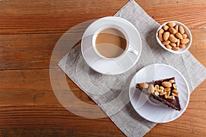 Chocolate cake with caramel, peanuts and almonds on a brown wooden background