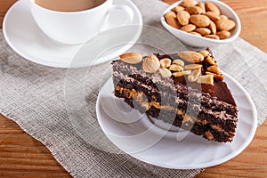 Chocolate cake with caramel, peanuts and almonds on a brown wooden background