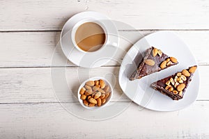 Chocolate cake with caramel, peanuts and almonds on a white wooden background