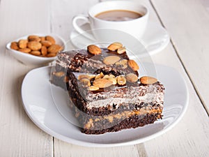 Chocolate cake with caramel, peanuts and almonds on a white wooden background