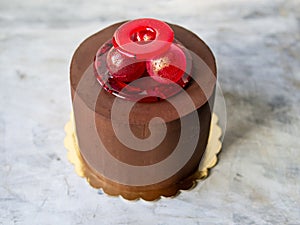 Chocolate cake covered with ganache with isomalt decor on marble gray background. Unusual decor of red isomalt - rings