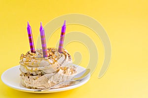 Chocolate cake with cream and three candles on a yellow background