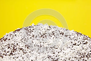Chocolate cake decorated with flaked coconut, homemade pie on yellow background, closeup. Home cake with cocoa ingredient and