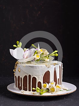 Chocolate cake decorated with flowers and poured white icing on black stone background