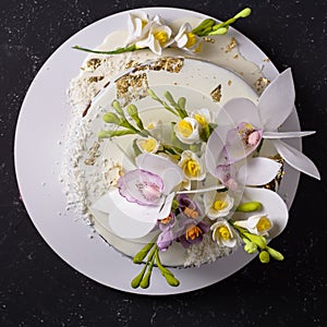 Chocolate cake decorated with flowers and poured white icing on black stone background. Top view. Flat lay photo