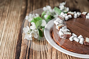 Chocolate cake, decorated with marshmallow, nougat, jasmine flowers on brown wooden table