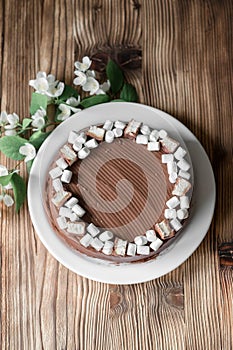 Chocolate cake, decorated with marshmallow, nougat, jasmine flowers on brown wooden table