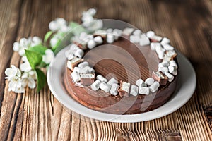 Chocolate cake, decorated with marshmallow, nougat, jasmine flowers on brown wooden table