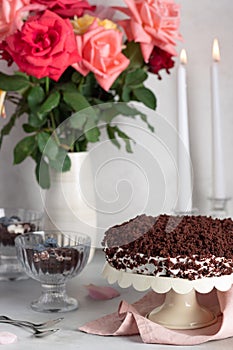 Chocolate cake on festive background with bouquet of roses and candles.