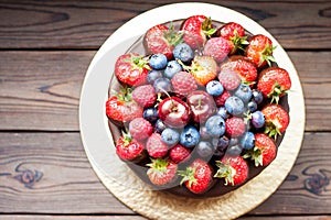 Chocolate cake with fresh summer berries, strawberries, raspberries, blueberries and cherries. Rustic wooden background