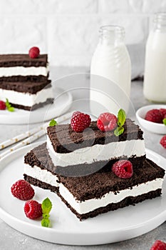 Chocolate cake with milk cream filling on a white plate with fresh raspberries and mint with bottles of milk. Delicious dessert.
