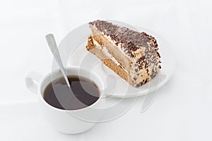 Chocolate cake slice with curl on white dish with hot drink