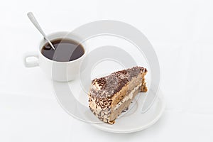 Chocolate cake slice with curl on white dish with hot drink