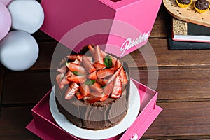 Chocolate cake with strawberries, basil leaves, blackberry jam and chocolate plates around. Next to balloons and brigadier. photo