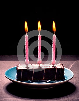 Chocolate cake with three pink candles on blue plate