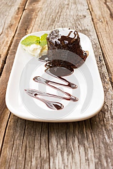 Chocolate cake with whipping cream on white plate. Over wooden t