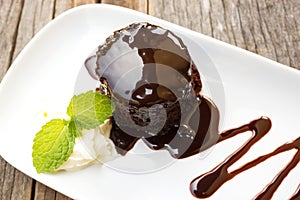 Chocolate cake with whipping cream on white plate. Over wooden t