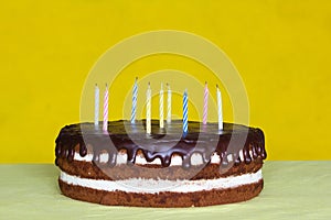 Chocolate cake with white cream and chocolate drops and candies on yellow background