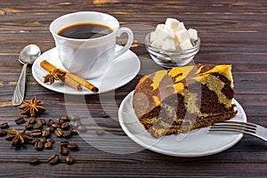 A chocolate cake on a white plate with a fork and a cup of black tea. A tea spoon. anise, coffee beans and a bowl of sugar cubes o