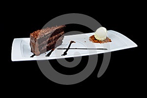 Chocolate cake on a white plate with ice cream on a black background