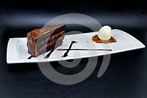 Chocolate cake on a white plate with ice cream on a black background