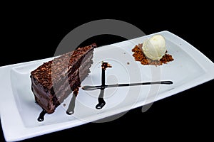 Chocolate cake on a white plate with ice cream on a black background
