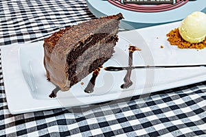 Chocolate cake on a white plate with ice cream on a black and white checkered tablecloth