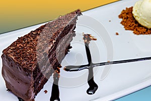 Chocolate cake on a white plate with ice cream on a yellow and light blue background