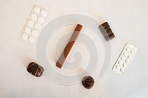Chocolate candies and pills lie on a white table