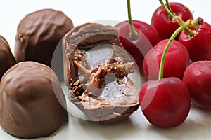 Chocolate candies with starchy corn syrup and condensed milk on a white plate with ripe, puff, juicy sweet cherry berries