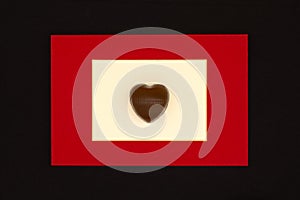 Chocolate candy in the form of a heart in a red frame on a black background. The concept of love