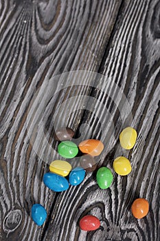 Chocolate candy in multi-colored glaze. Scattered on black pine boards