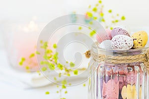 Chocolate Candy Multi-Colored Small Quail Easter Eggs Pastel Colors in Vintage Glass Jar on White Wood Table Yello Flowers