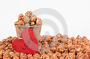 Chocolate caramel popcorn in paper bucket on white background. Popcorn and red heart.