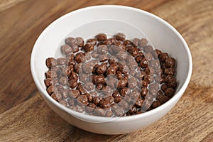 Chocolate cereal balls with milk in white bowl for breakfast on wooden table
