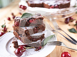 Chocolate cherry cake. Served stacked and sliced on a plate on light wooden table