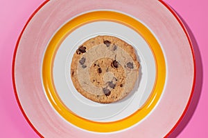 Chocolate chip cookie on a bright plate, pink backdrop.