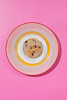 Chocolate chip cookie on a bright plate, pink backdrop.