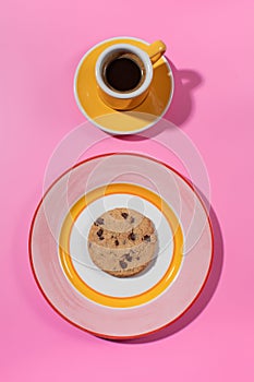 Chocolate chip cookie on a bright plate, pink backdrop with a cup of coffee.