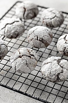 Chocolate chip cookies with cracks. Metallic rack with fresh baked chocolate crinkle cookies in icing sugar on gray