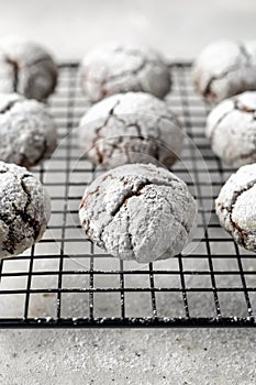 Chocolate chip cookies with cracks. Metallic rack with fresh baked chocolate crinkle cookies in icing sugar on white