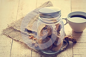 Chocolate chip cookies in glass jar on sack and coffee on wooden