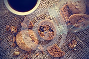 Chocolate chip cookies in glass jar on sack and coffee on wooden