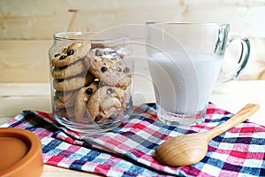 Chocolate chip cookies in glass jars with milk on wooden background