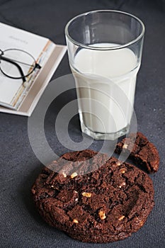 Chocolate chip cookies with a glass of milk on the background of an open book on a gray table