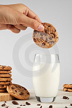 Chocolate chip cookies and a glass of milk on a light background. The cookie is dipped in milk.