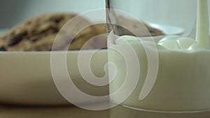 Chocolate chip cookies and milk being poured in a glass. Close up super slow motion shot