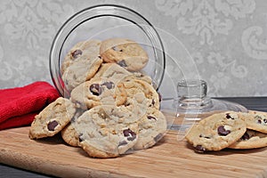 Chocolate chip cookies spilling out of a glass cookie jar.